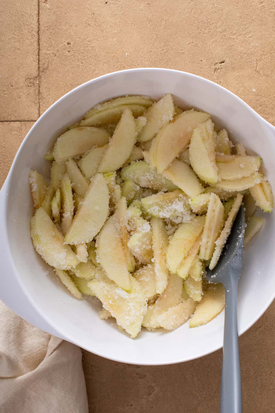 Sliced apples mixed with sugar in a white bowl.