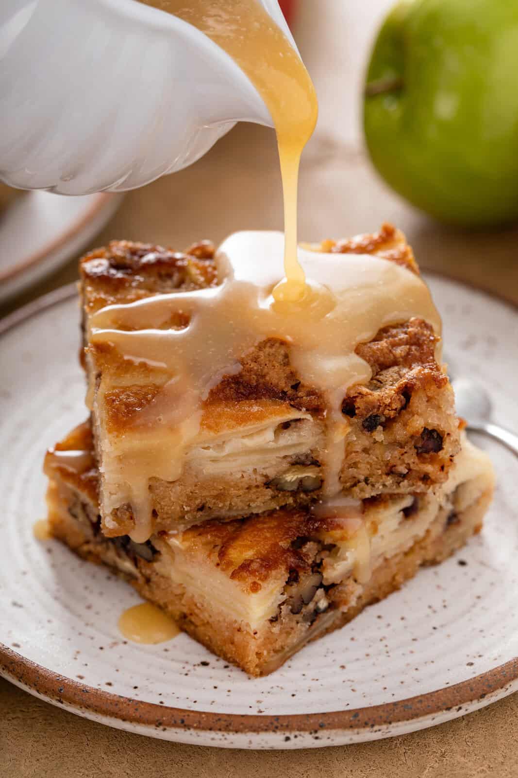 Dessert sauce being poured over two sliced slices of apple cake.