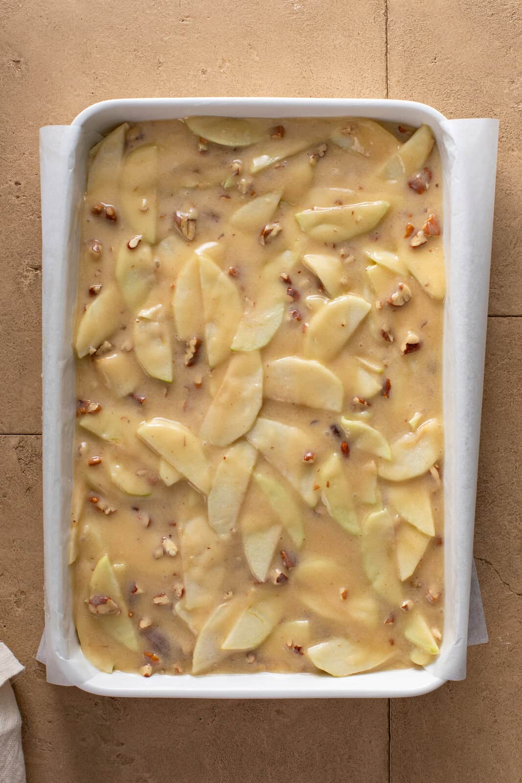 Fresh apple cake batter spread into a cake pan, ready to go in the oven.