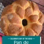 Baked loaf of pan de muerto cooling on a wire rack. Text overlay includes recipe name.