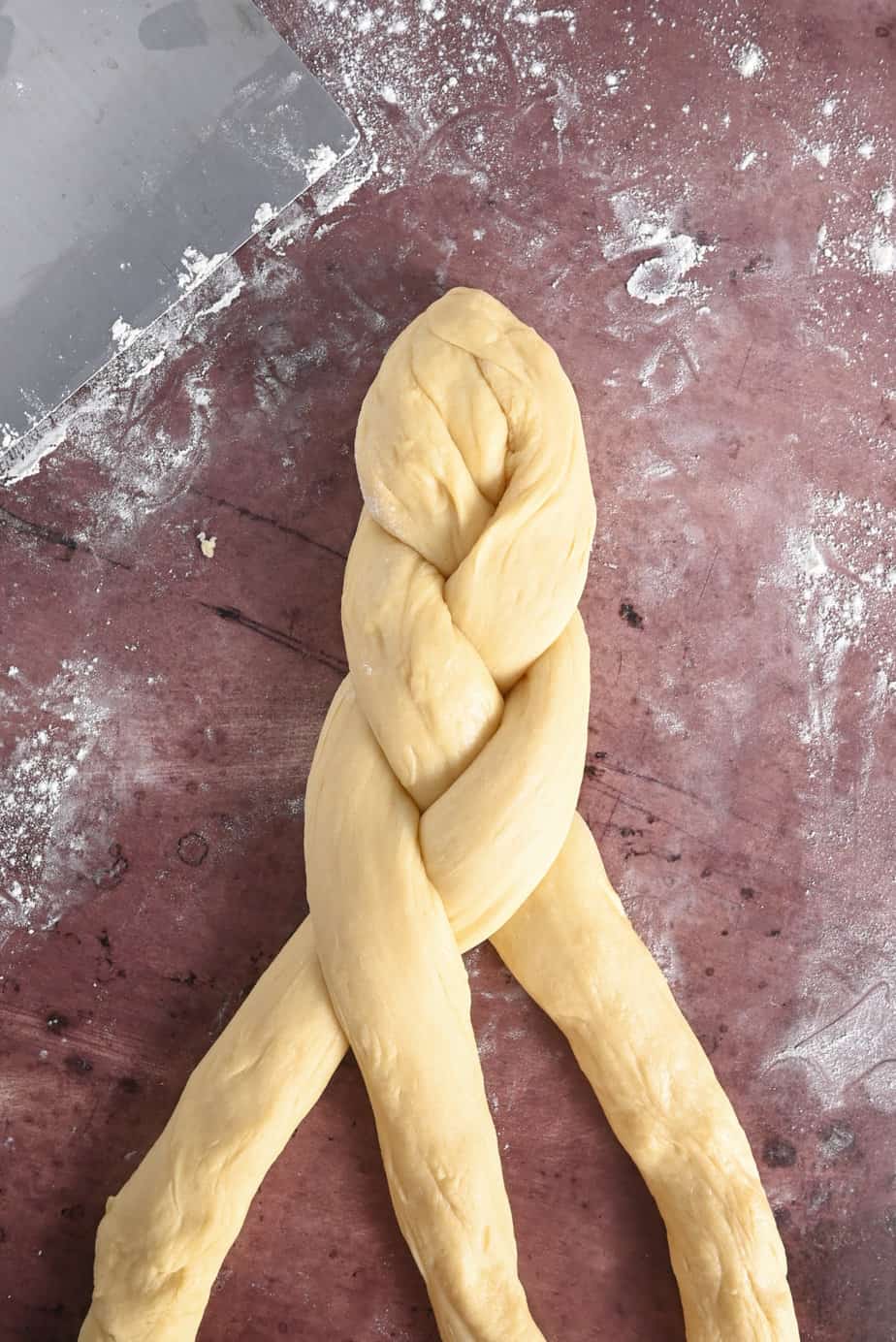 Pan de muerto dough being braided on a floured surface.