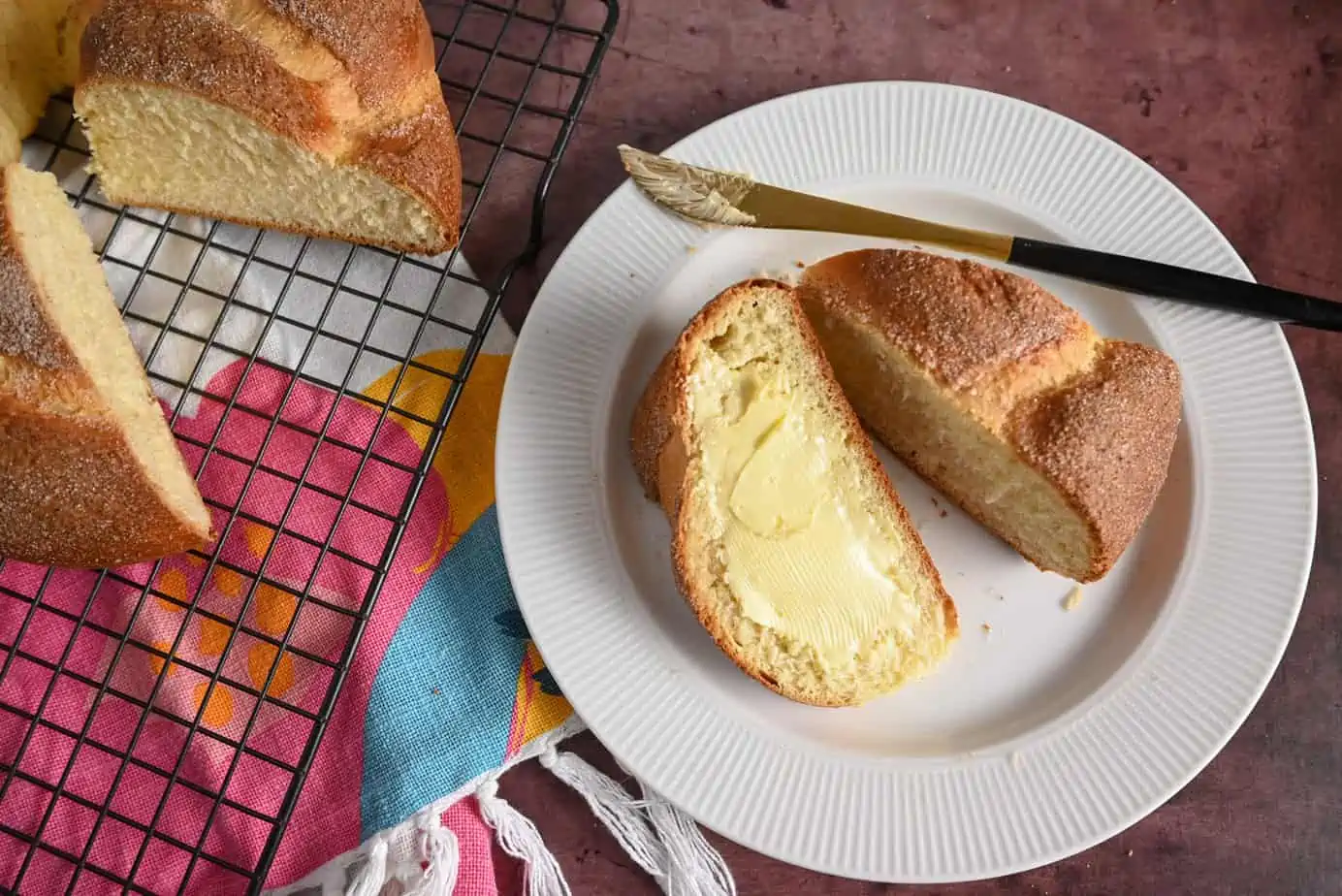 Two slices of pan de muerto on a white plate. Once piece has been topped with softened butter.