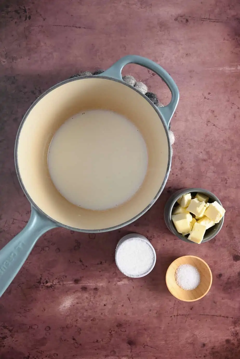 Scalded milk in a saucepan next to butter, sugar, and salt.