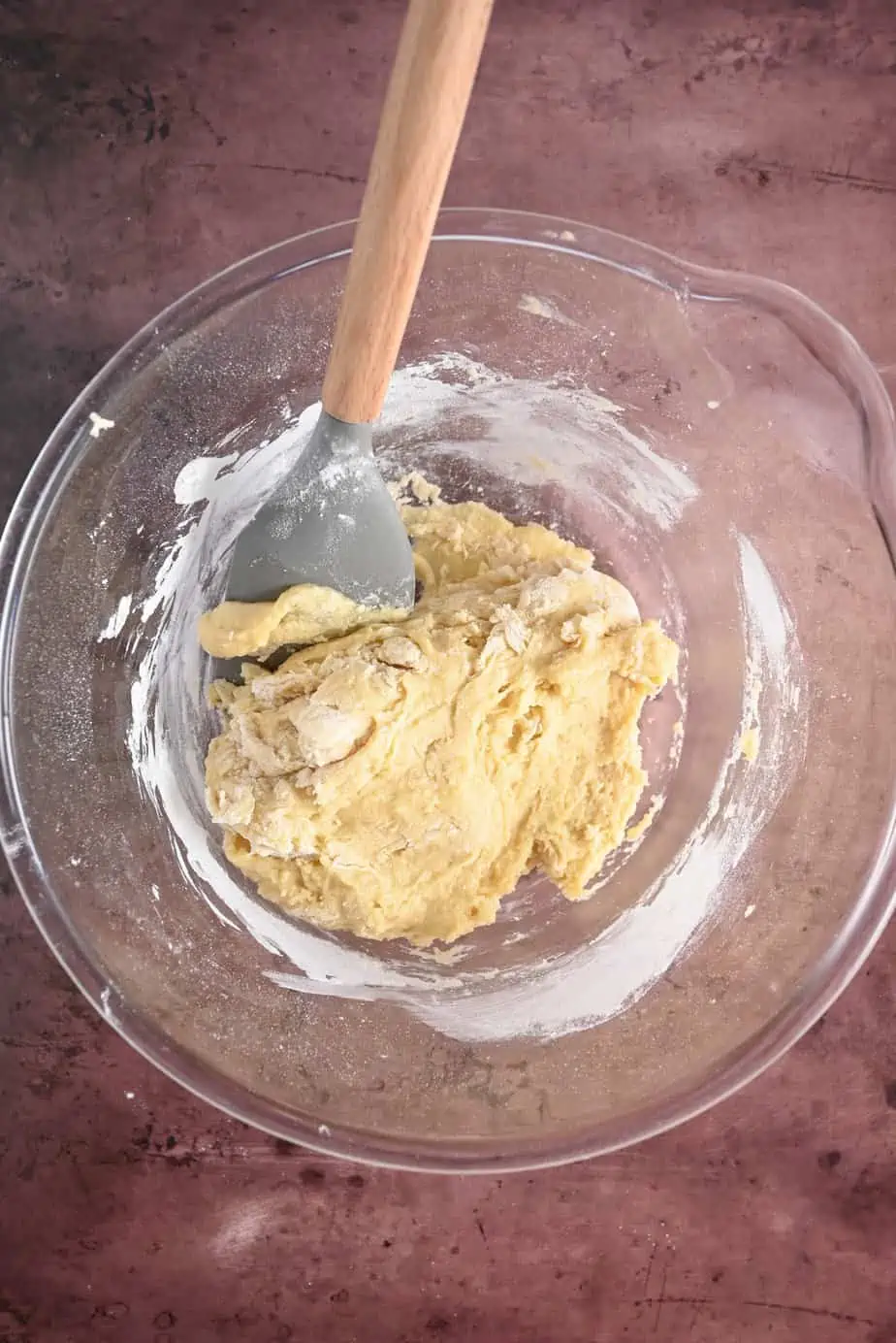 Spatula stirring pan de muerto dough in a glass bowl.