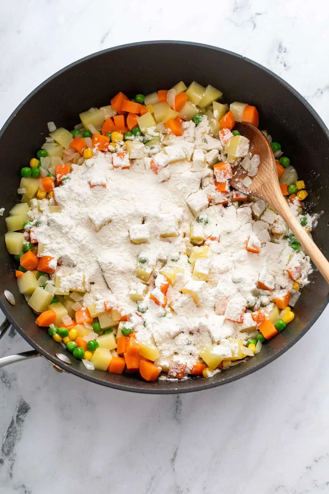 Flour sprinkled over cooked vegetables in a black skillet.