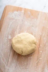 Ball of pie dough on a floured wooden cutting board.