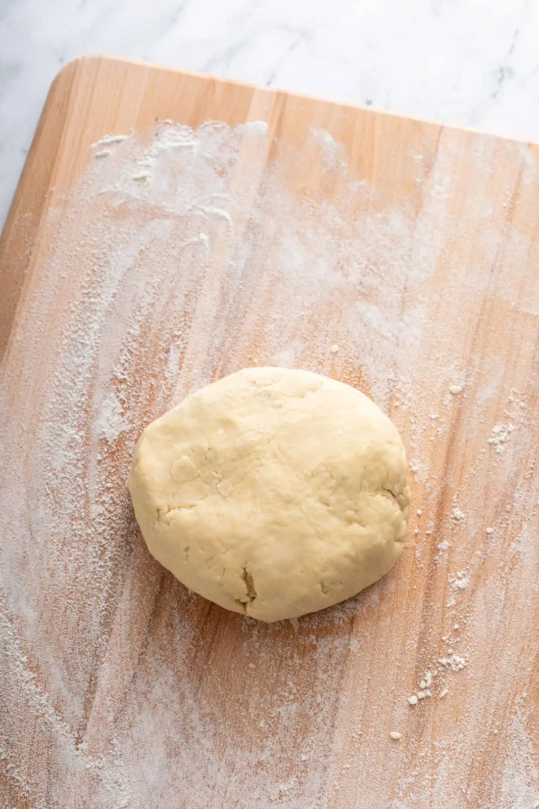 Ball of pie dough on a floured wooden cutting board.