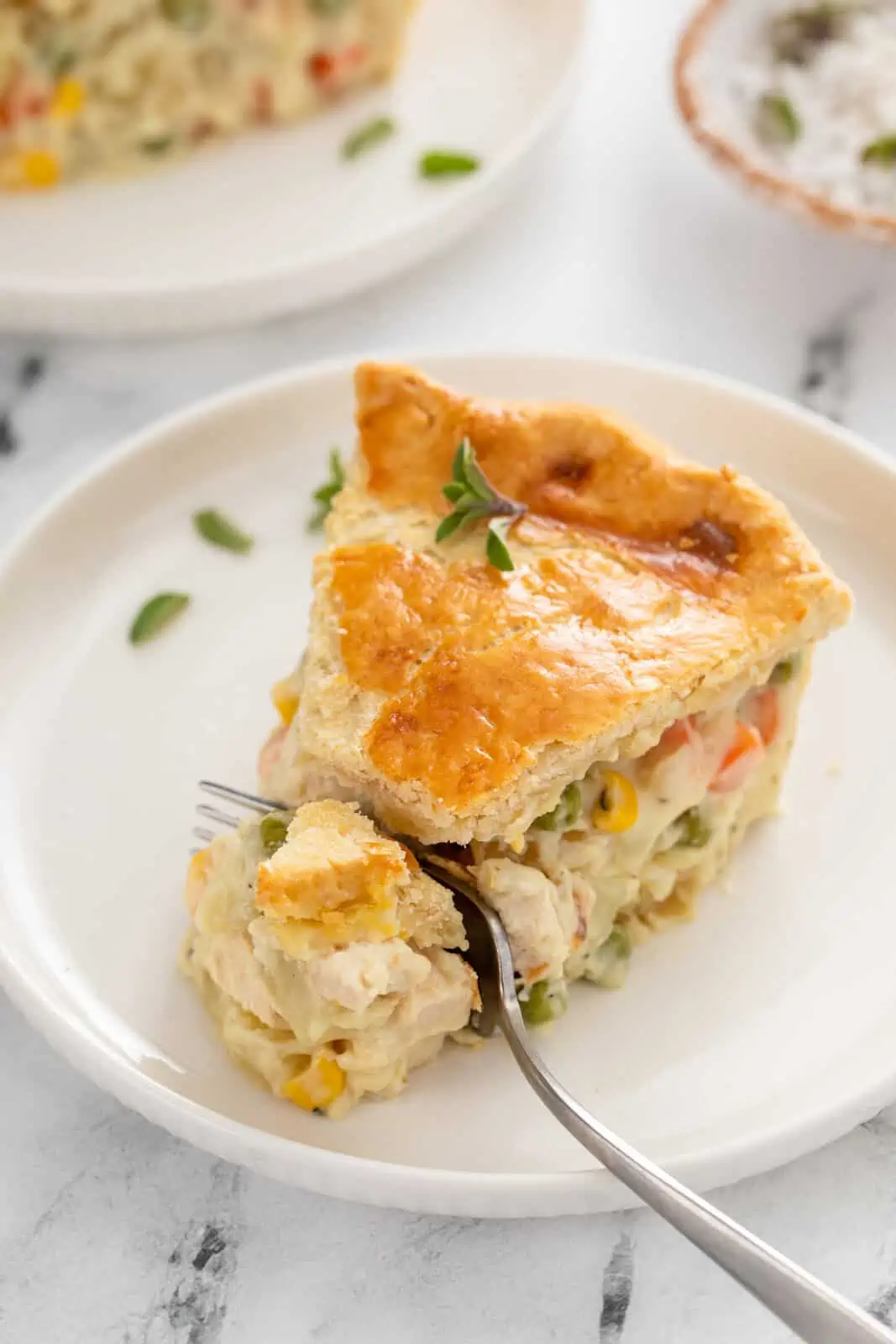 Fork cutting a bite from a slice of chicken pot pie on a white plate.