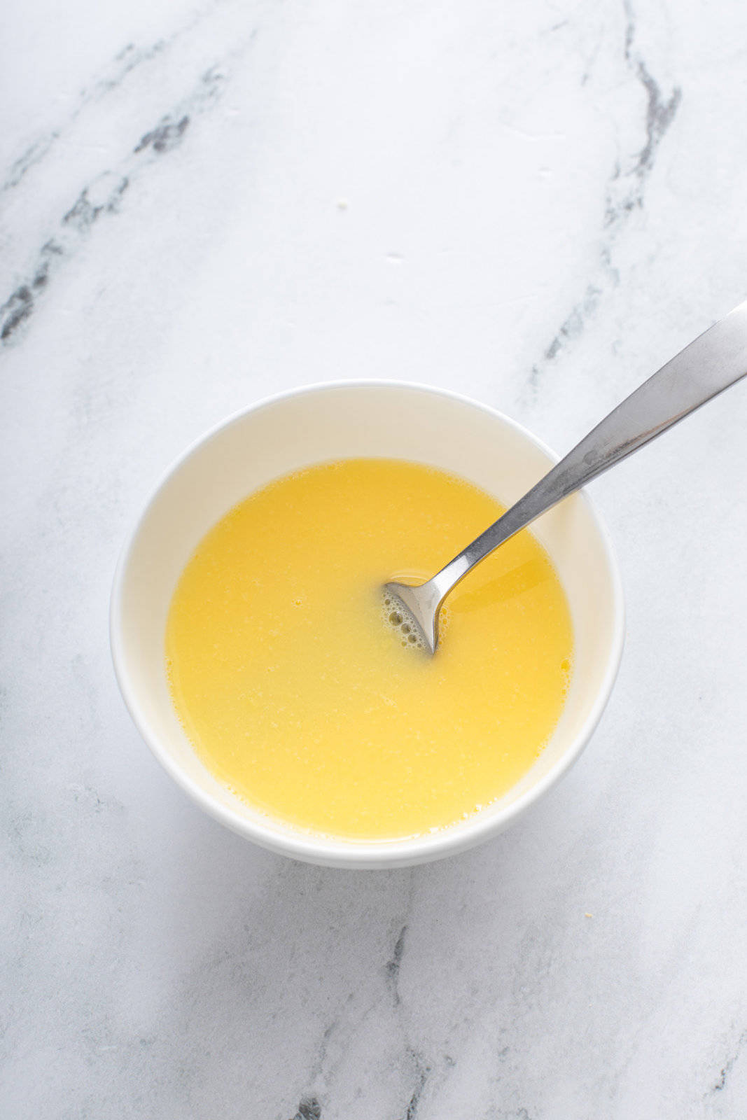 Egg wash in a white bowl on a marble countertop.
