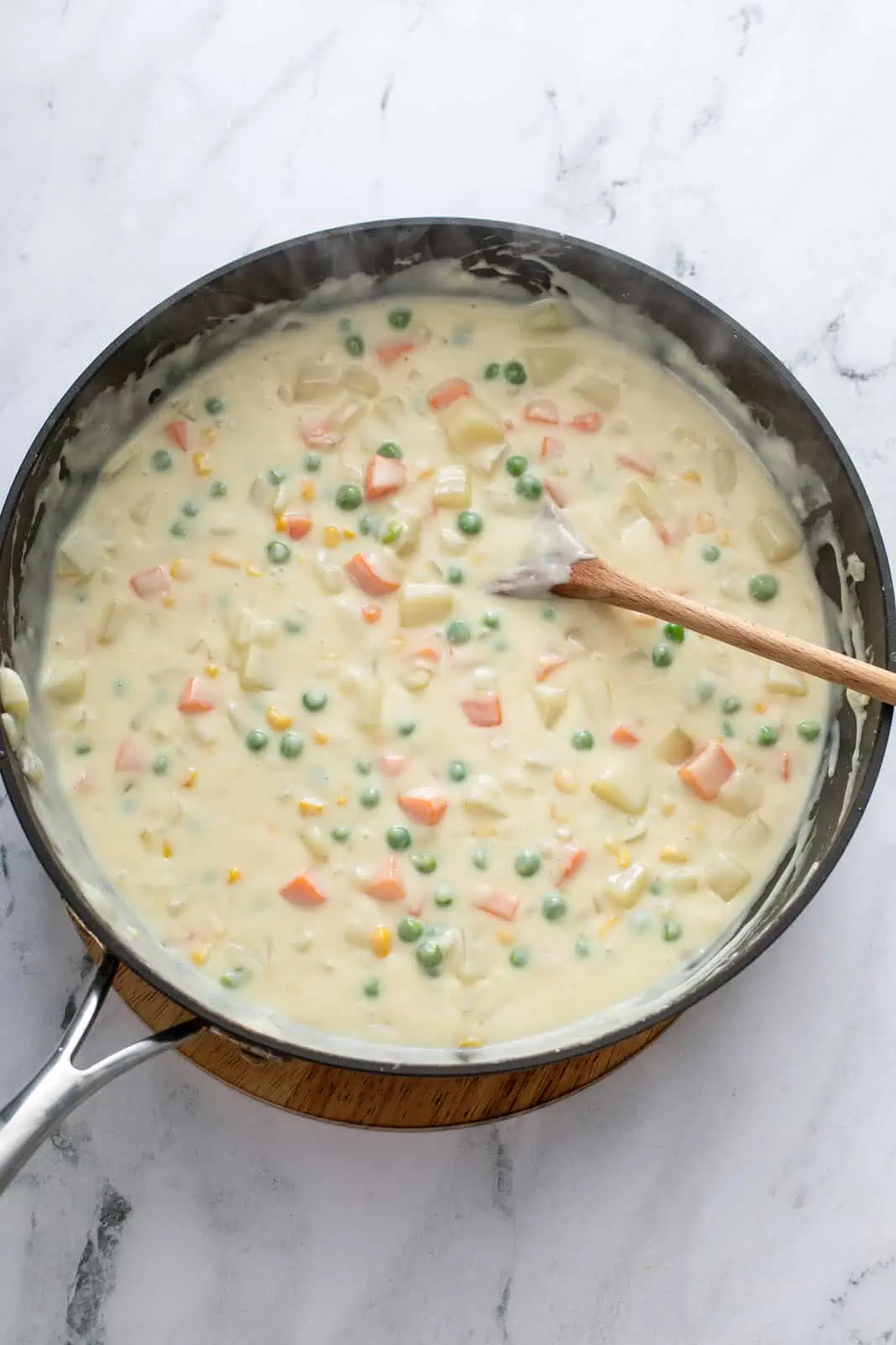 Cooked vegetables in a creamy sauce base in a black skillet.