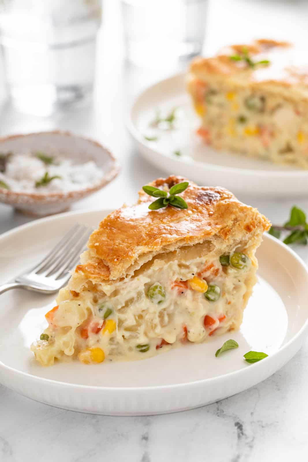 Slice of chicken pot pie next to a fork on a white plate.