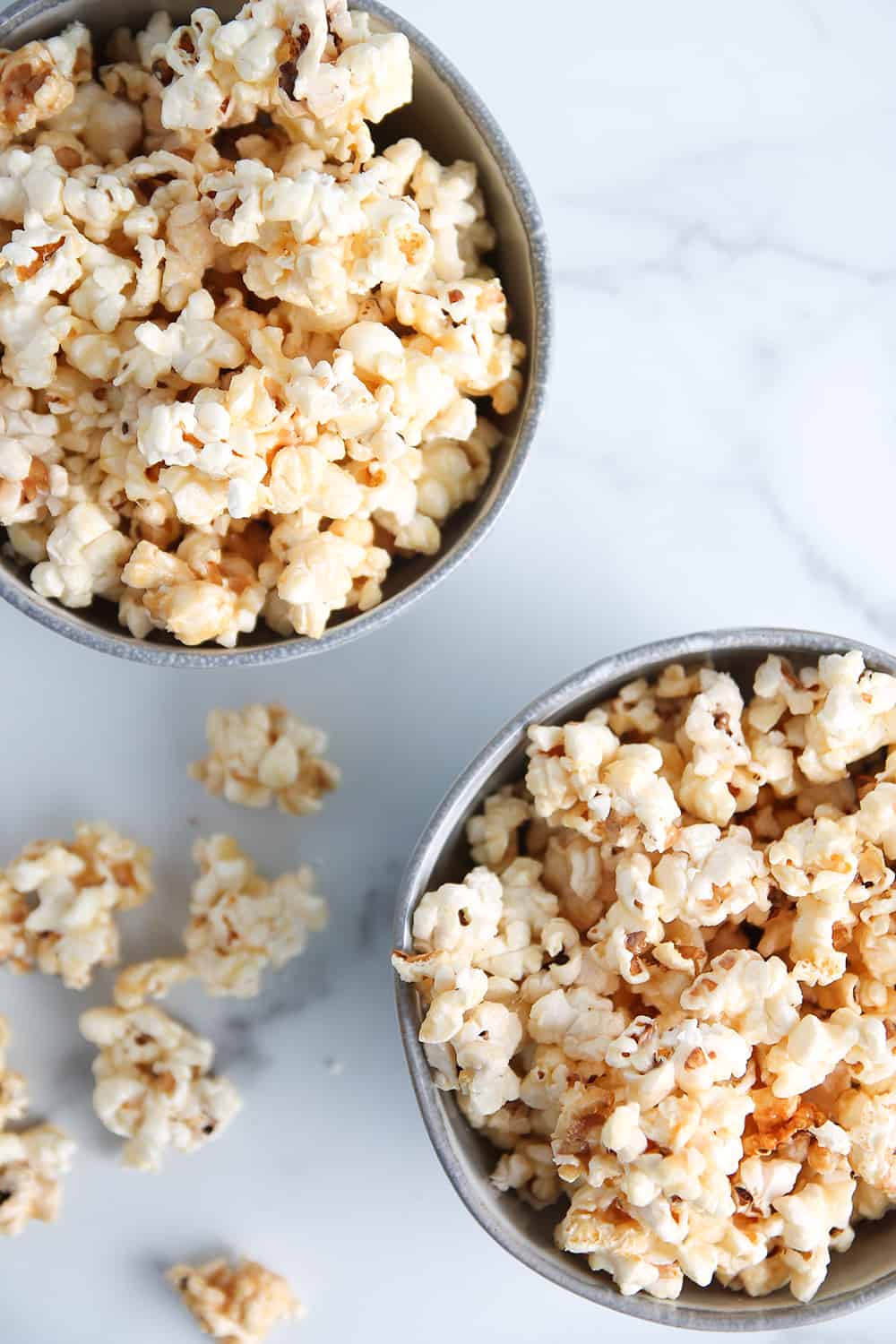 Two bowls of microwave caramel corn on a marble counter