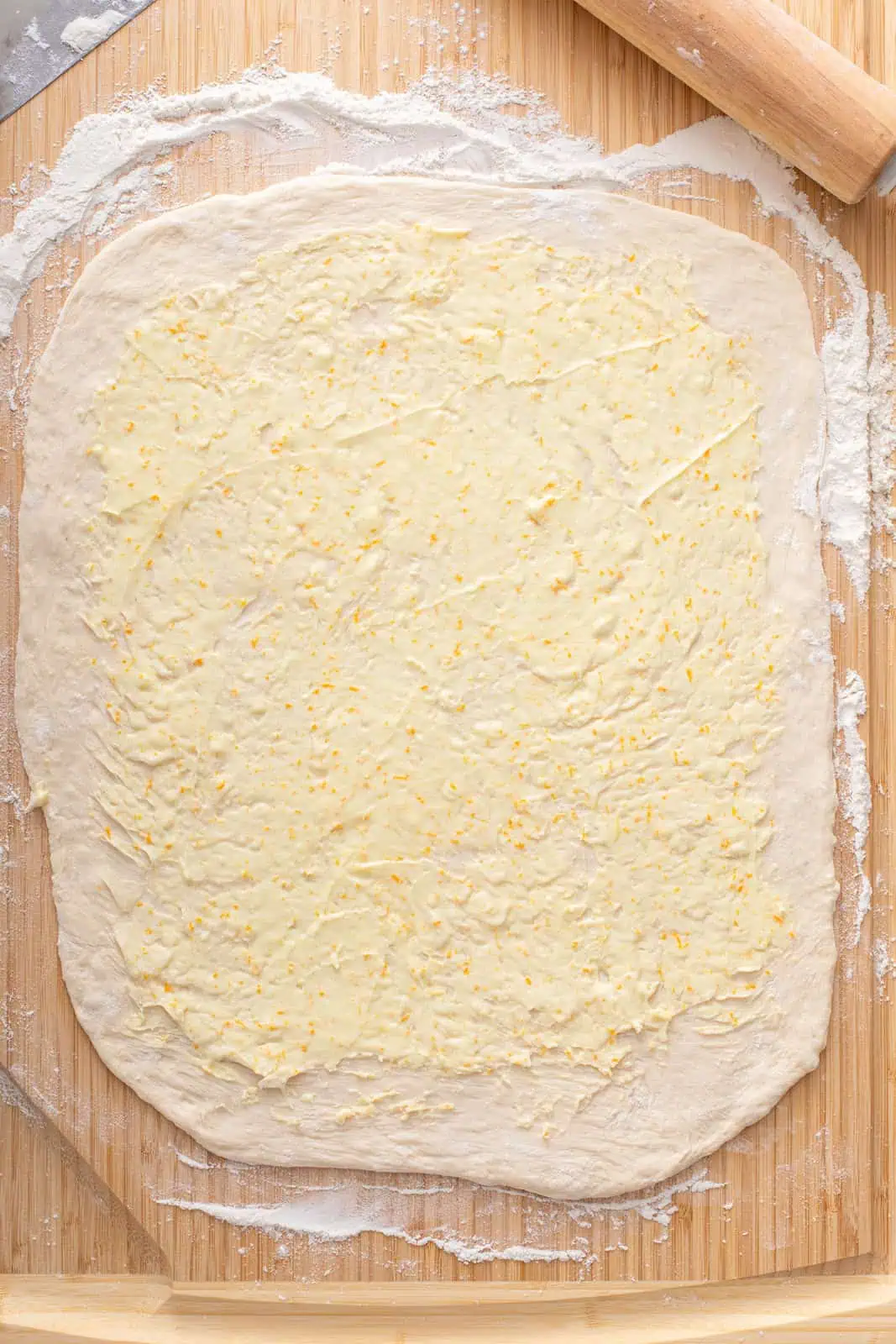 Orange icing spread over a rectangle of sweet roll dough.