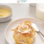 Frosted orange roll on a white plate with a glass of milk and the pan of rolls in the background. Text overlay includes recipe name.