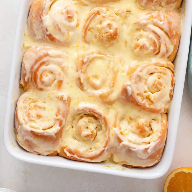 Frosted orange rolls in a white baking dish.