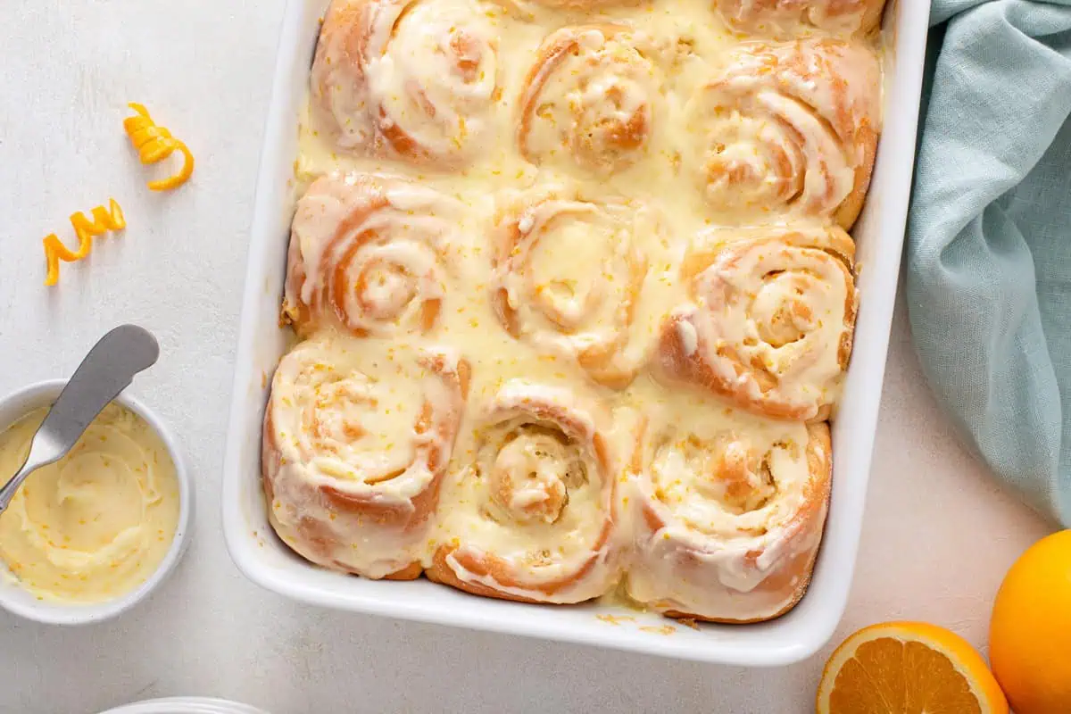 Overhead view of frosted orange rolls in a white pan.