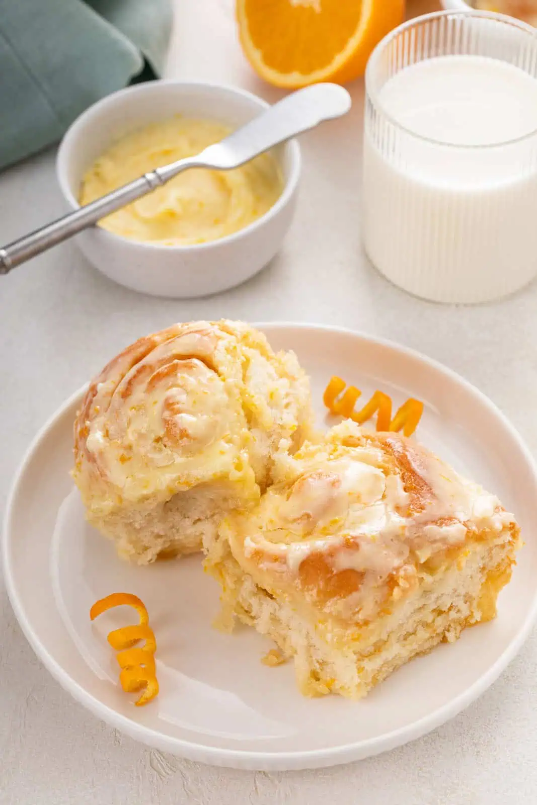 Two frosted orange rolls arranged on a white plate.