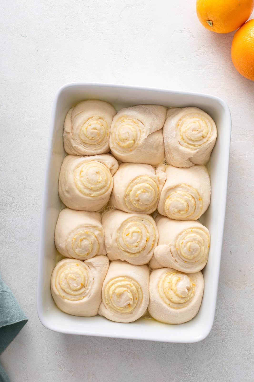 Risen orange rolls in a white baking dish, ready to go in the oven.
