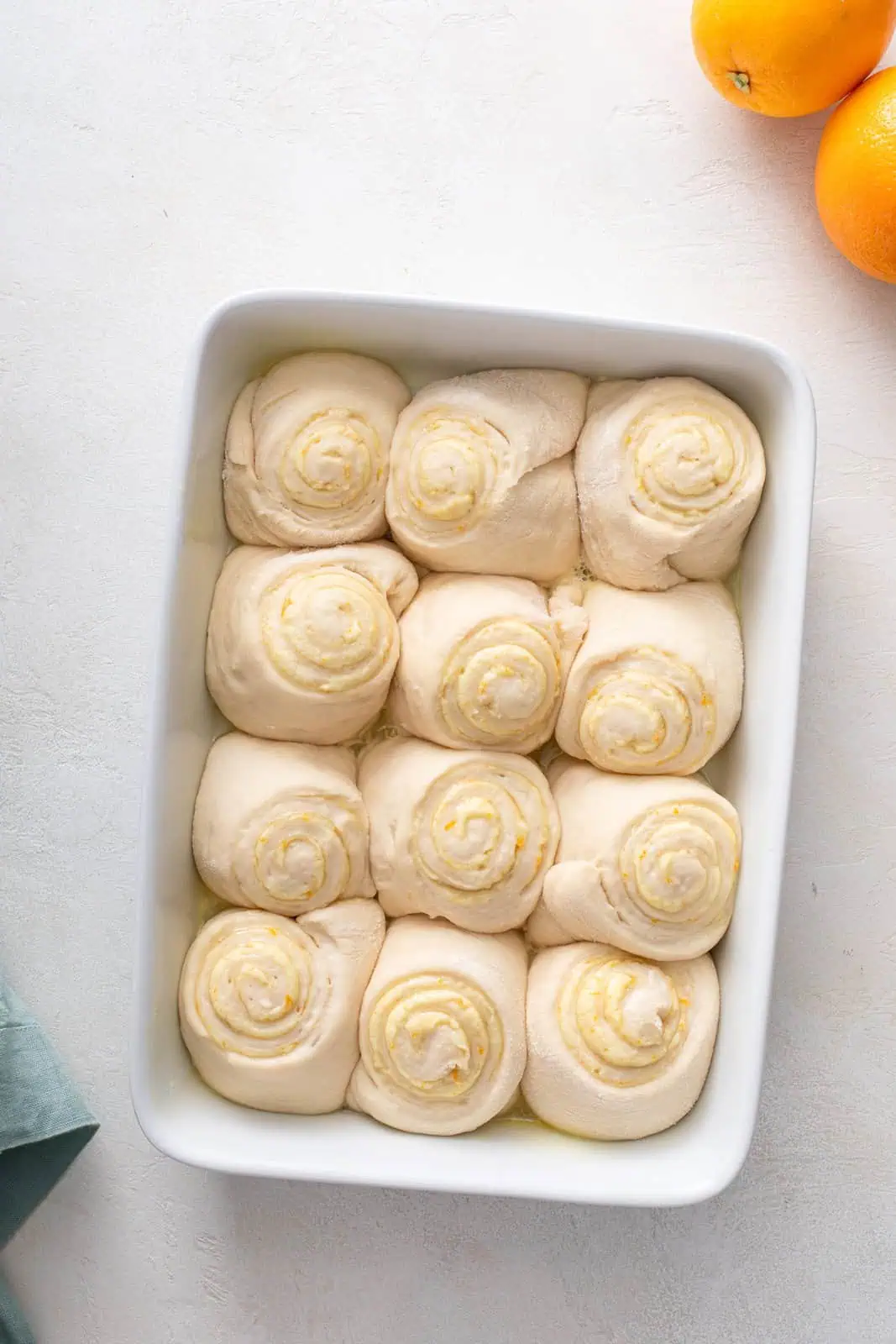 Risen orange rolls in a white baking dish, ready to go in the oven.