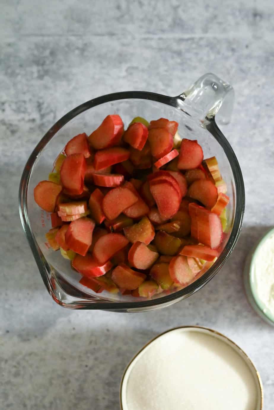 Chopped rhubarb in a large glass measuring cup, set on a gray countertop.