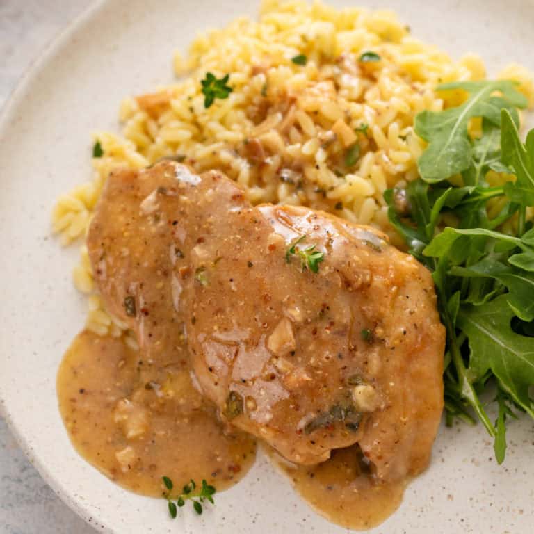 Close up of garlic chicken next to orzo and an arugula salad on a plate.
