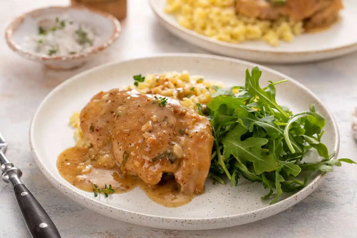 Plate filled with garlic chicken topped with sauce, orzo, and an arugula salad.