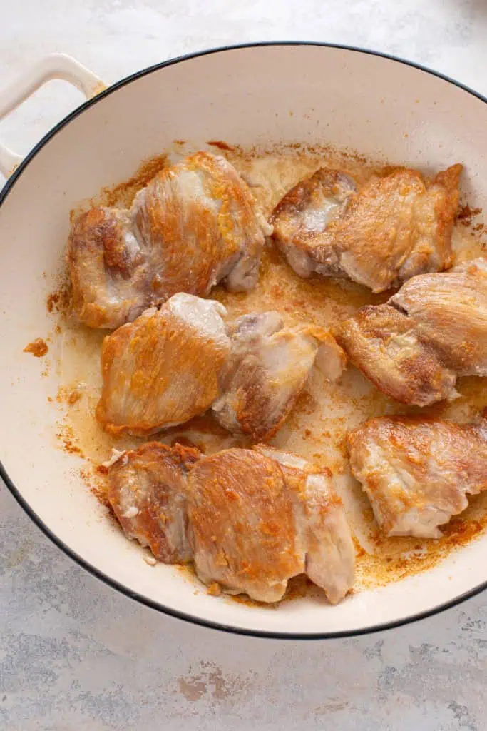Seared chicken thighs in an enameled cast iron skillet.