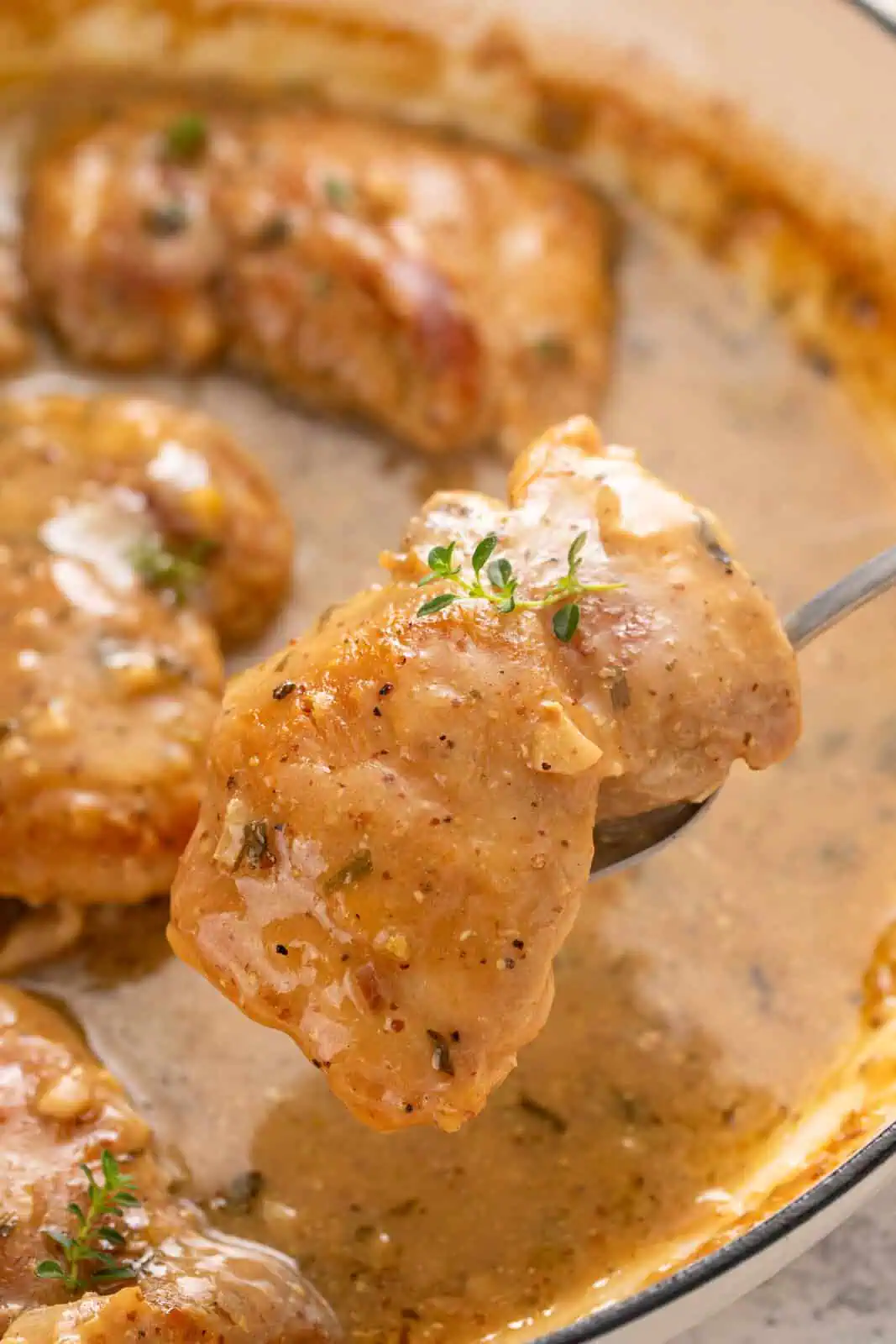 Spoon lifting up a garlic chicken thigh from a skillet.