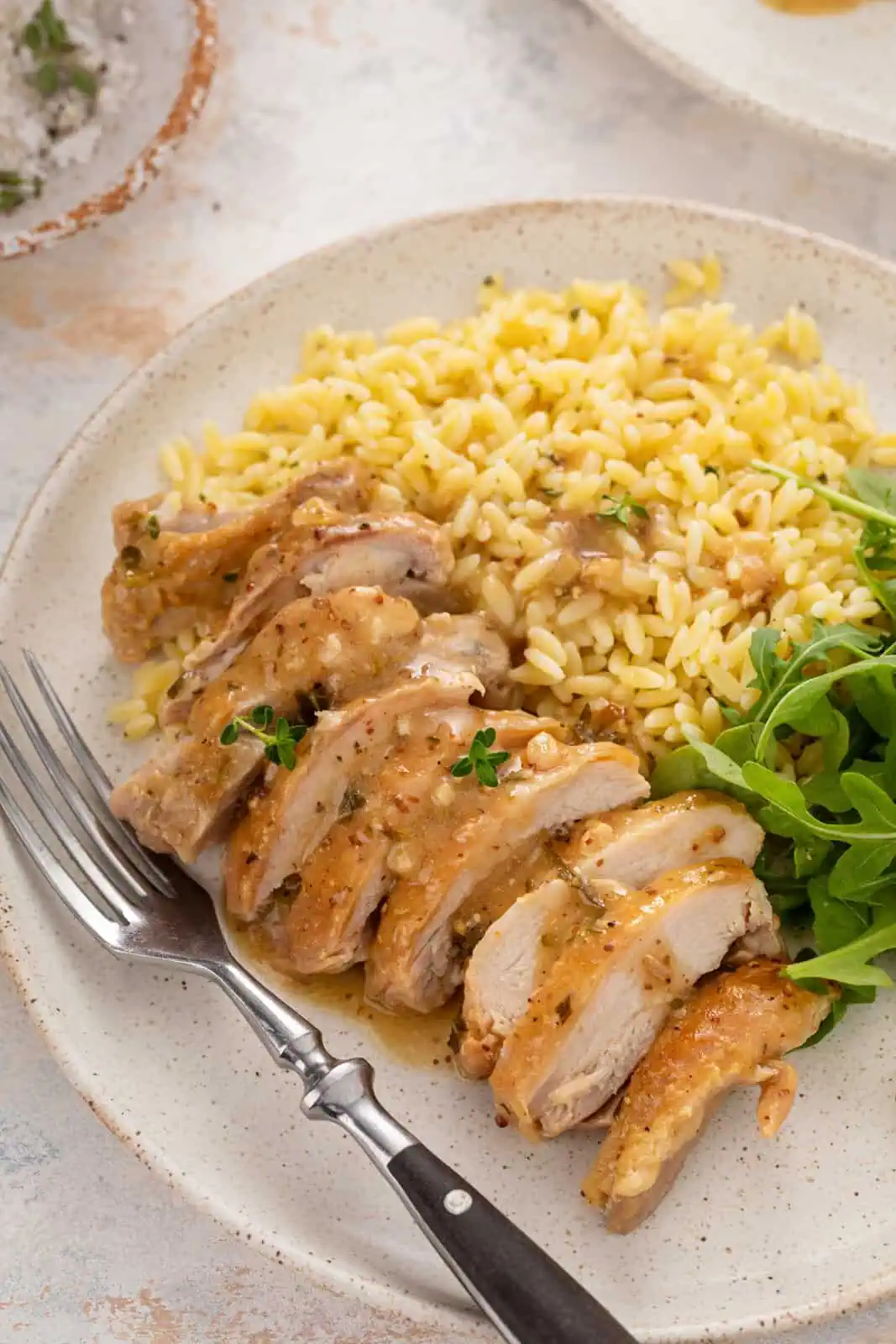 Sliced garlic chicken thigh with sauce next to orzo and an arugula salad on a plate.