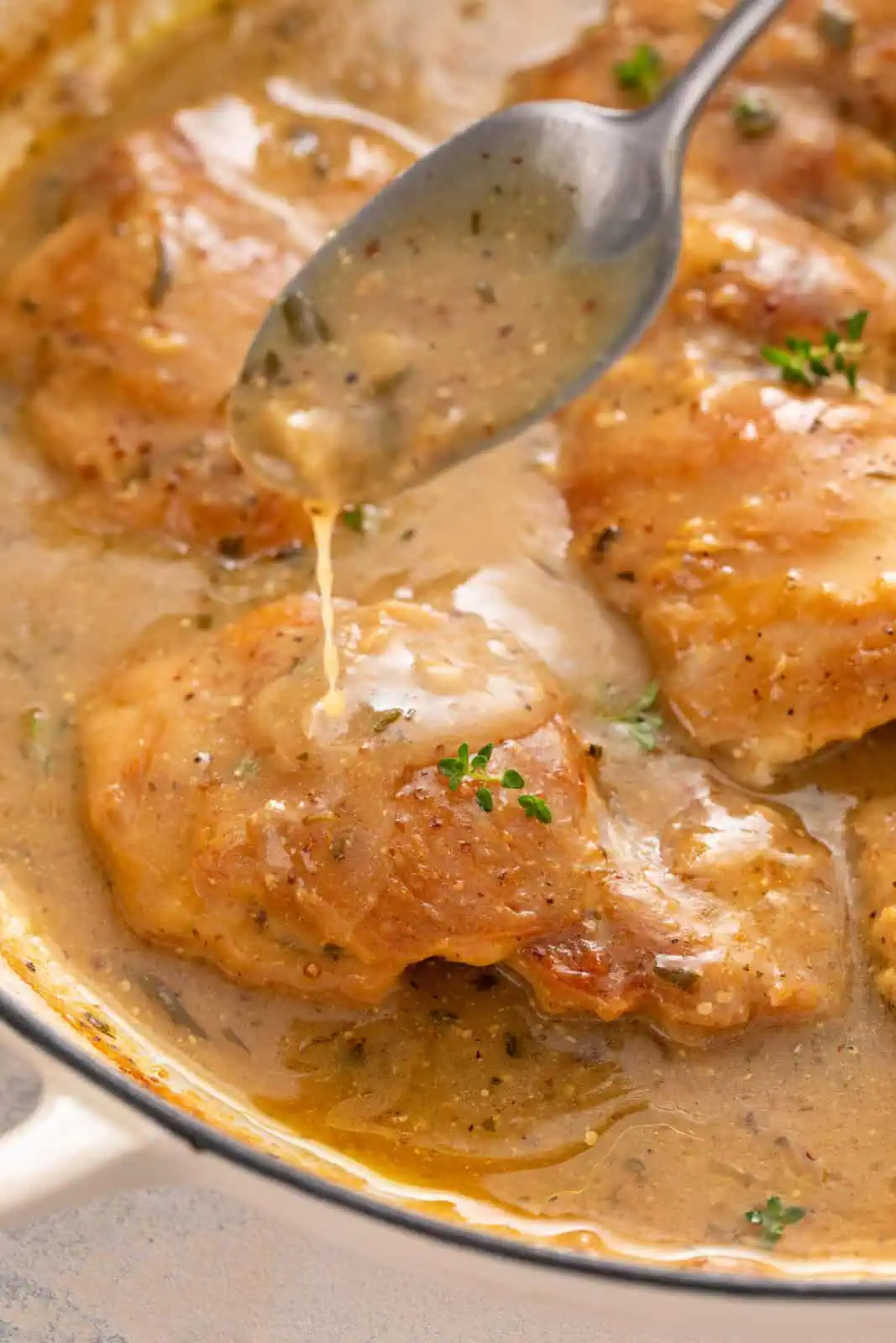 Spoon drizzling garlic sauce over chicken thighs in a skillet.