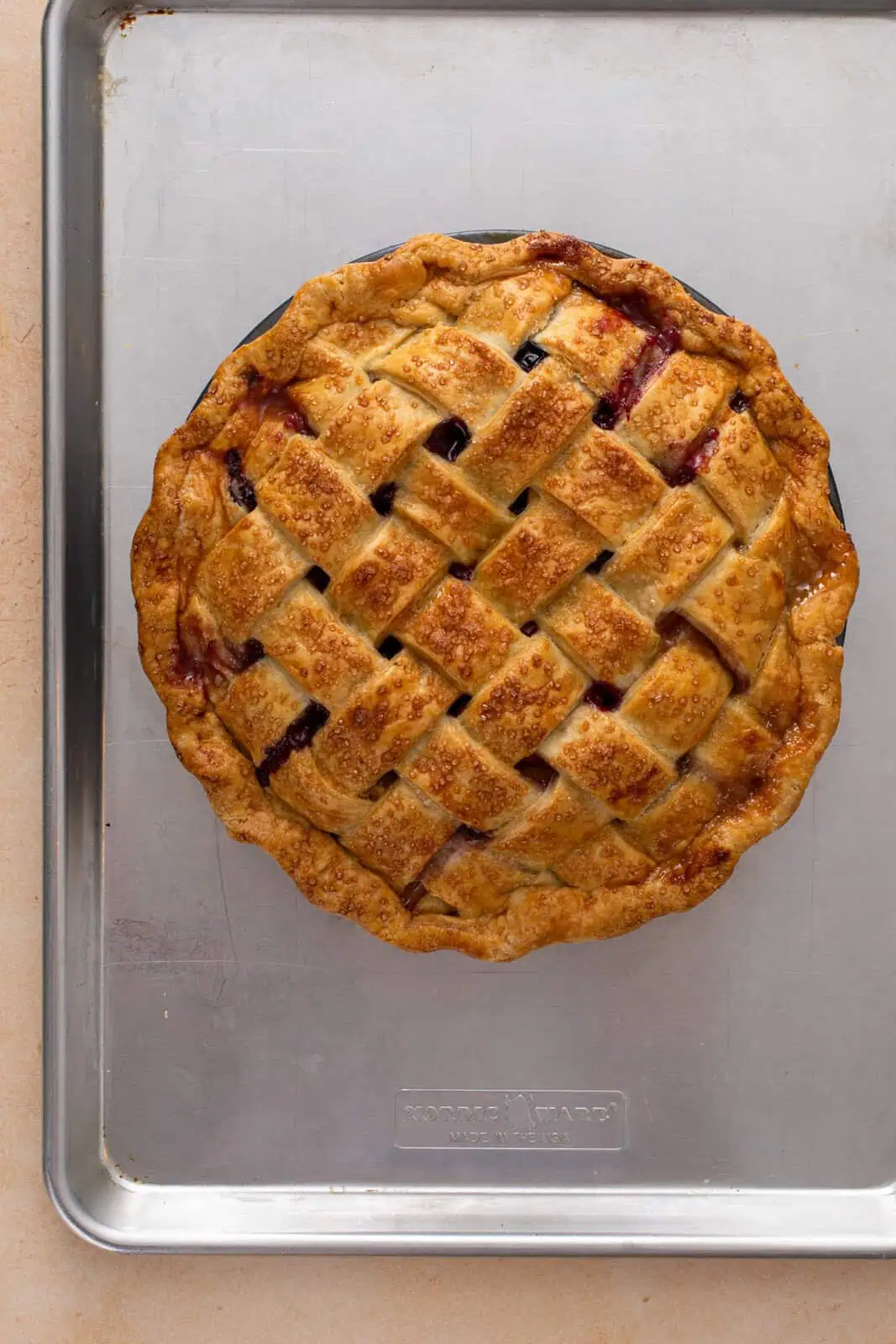 Golden, baked peach blueberry pie cooling on a baking sheet.