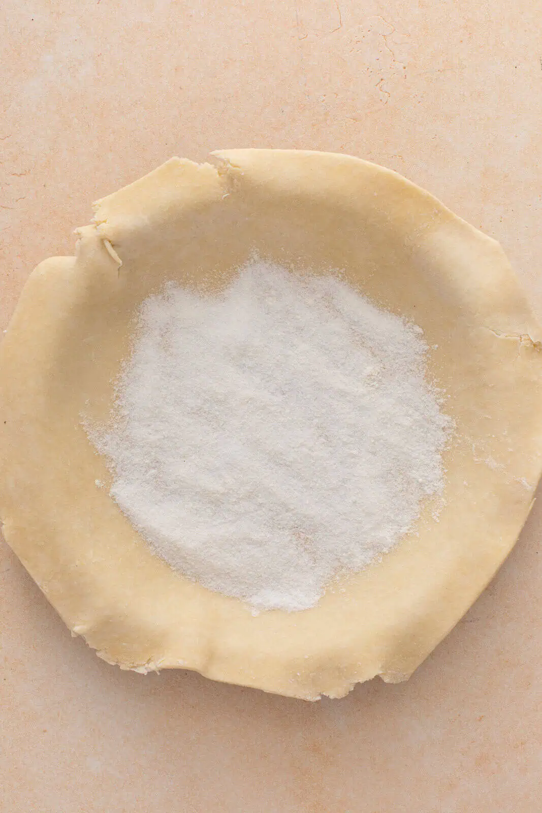 Flour and sugar mixture sprinkled in the bottom of a pie crust-lined pie plate.