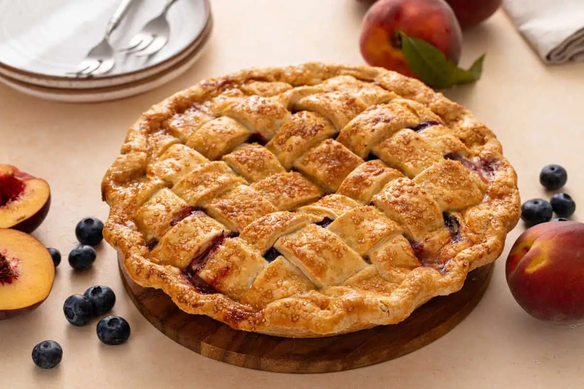 Cooled lattice-topped peach blueberry pie resting on a countertop.