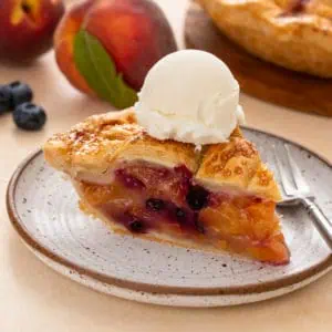 Slice of peach blueberry pie a la mode on a plate.