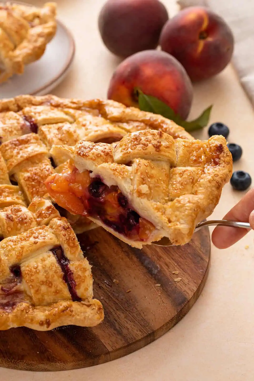 Hand lifting up a pie server holding a slice of peach blueberry pie.