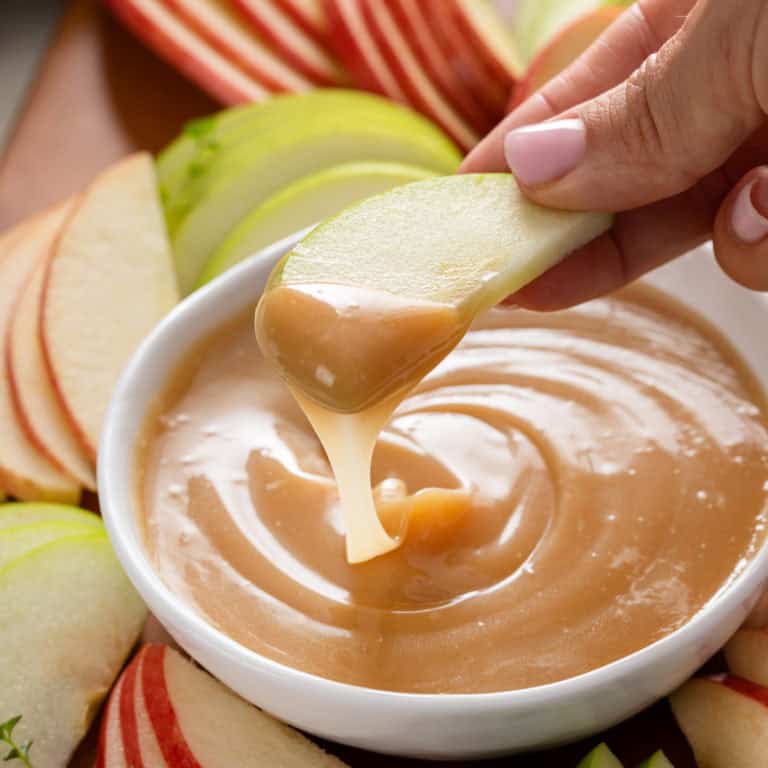 Hand holding up a slice of apple dipped in caramel apple dip.