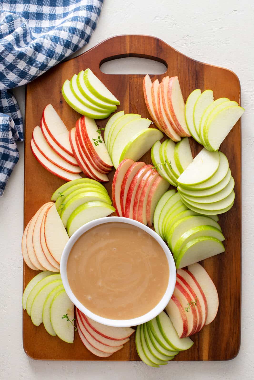 Overhead view of a bowl of apple dip surrounded by apple slices on a wooden board.