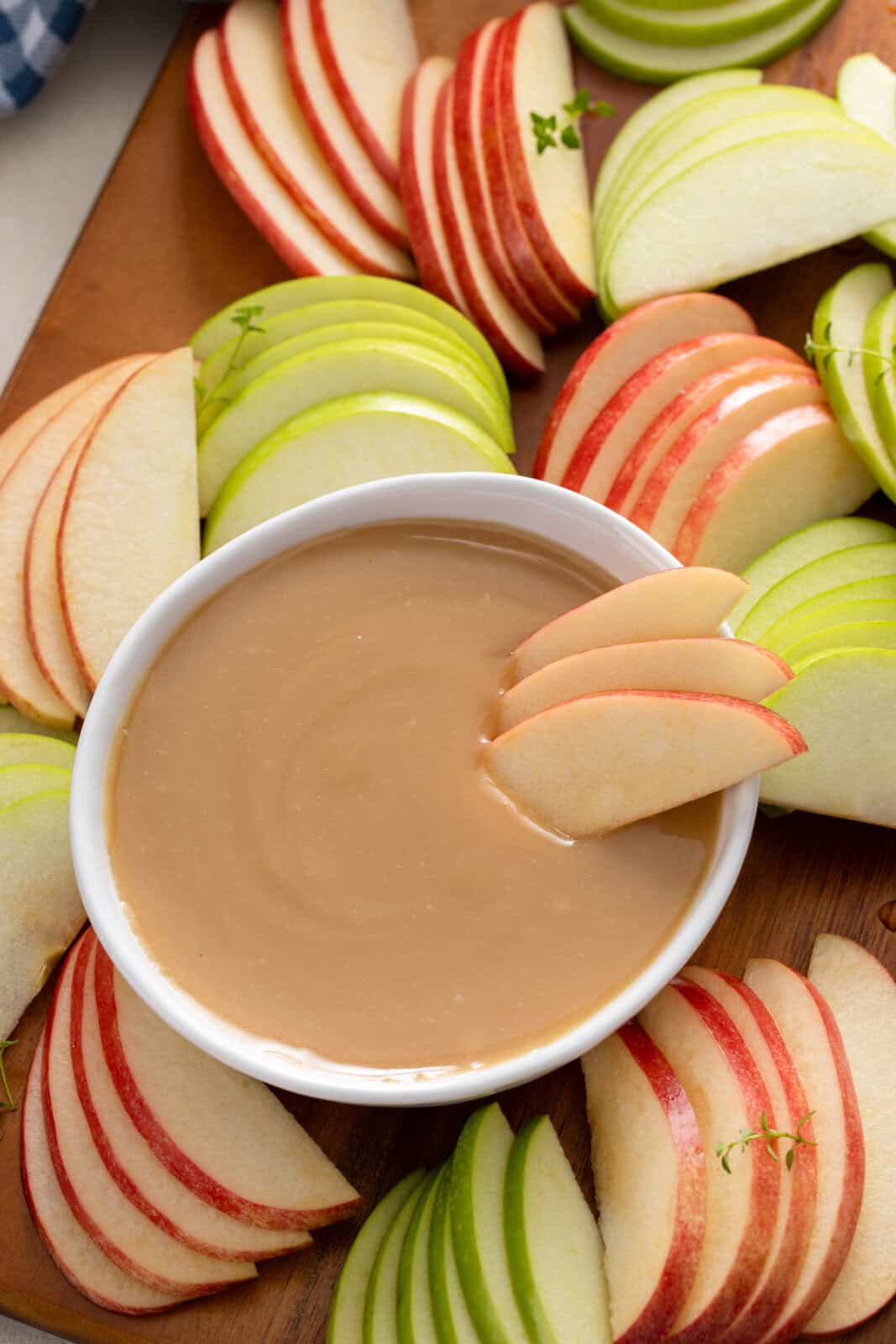 Apple slices arranged in a bowl of apple dip set on a board with sliced apples.