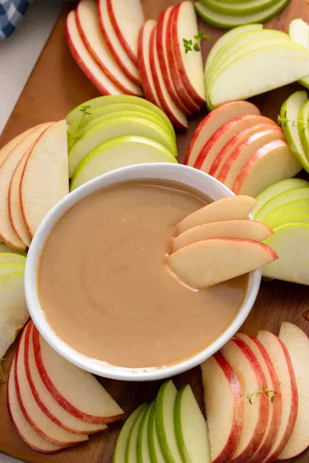 Apple slices arranged in a bowl of apple dip set on a board with sliced apples.