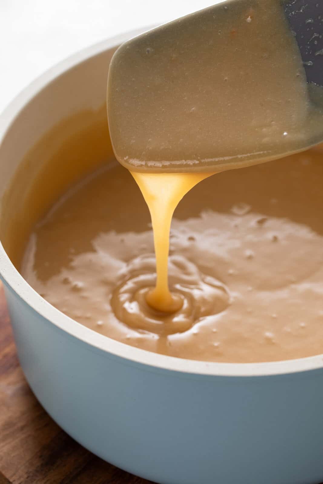 Spatula drizzling apple dip into a saucepan to show the texture.