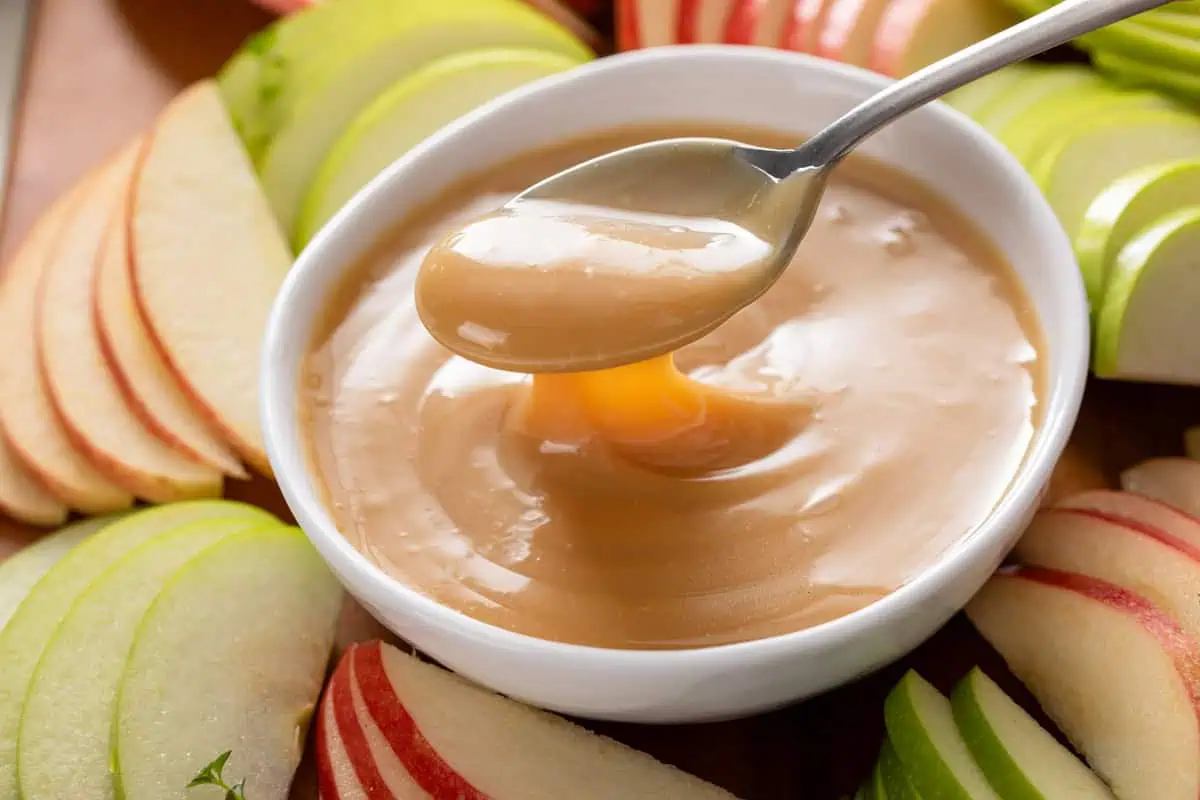 Spoon lifting a bite of apple dip out of a white bowl.