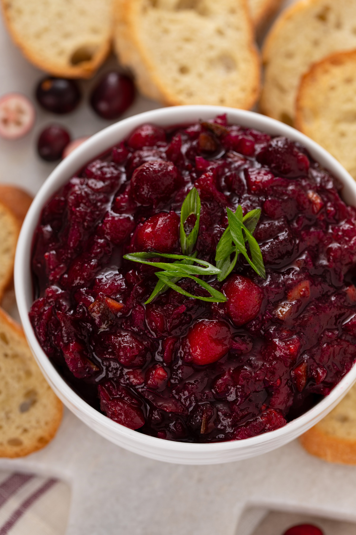 Overhead image of cranberry chutney in a white bowl, garnished with green onions.