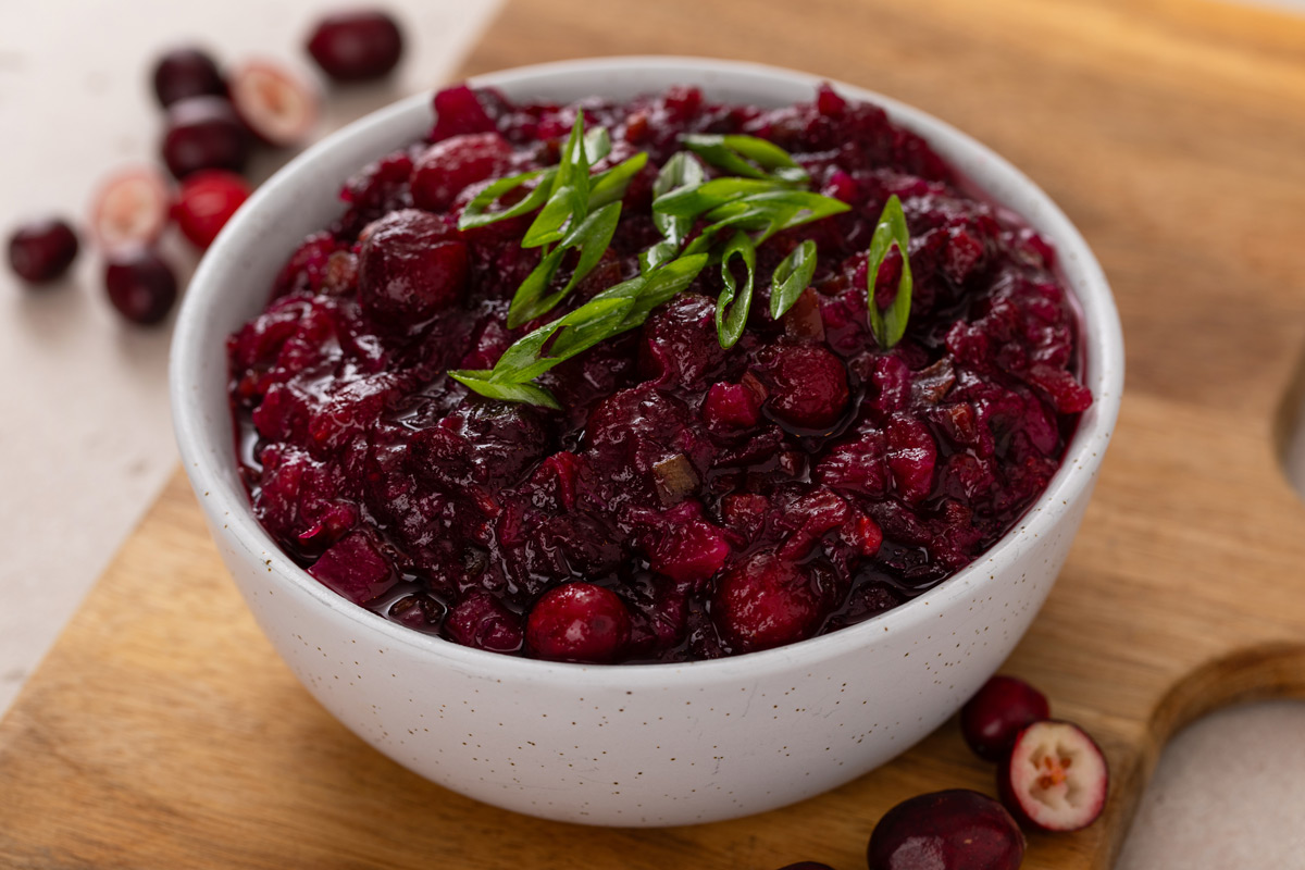 White bowl filled with cranberry chutney on a wooden board.