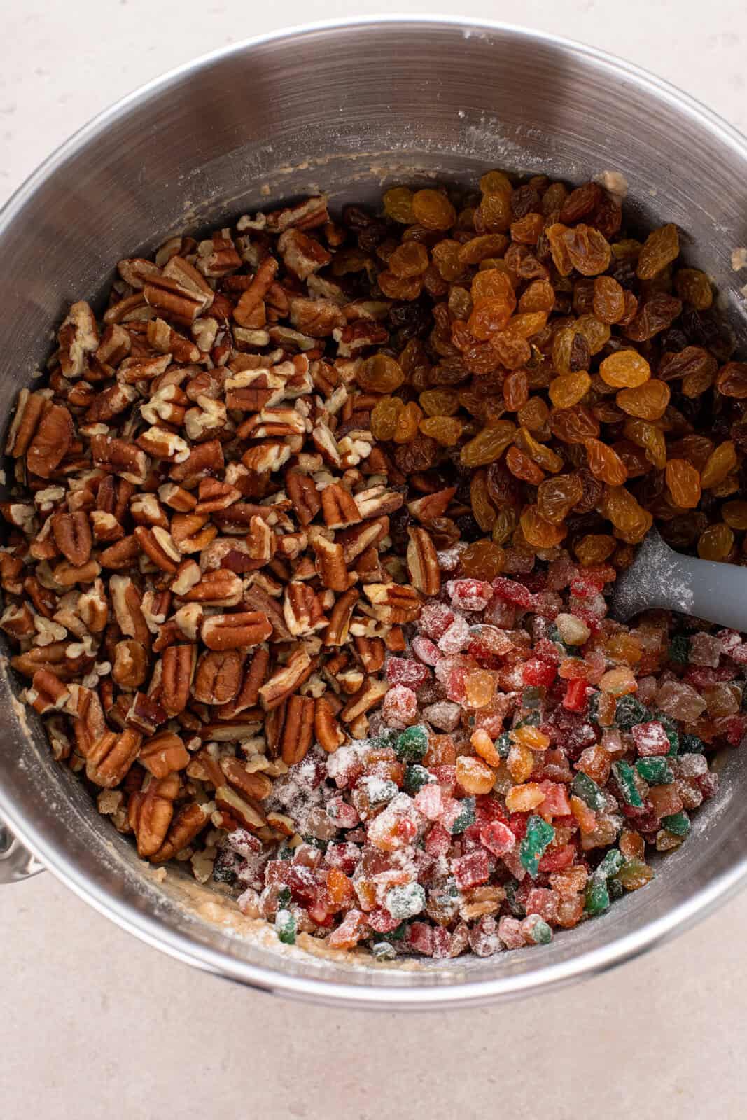 Chopped nuts, candied fruit, and raisins being added to fruitcake cookie dough.