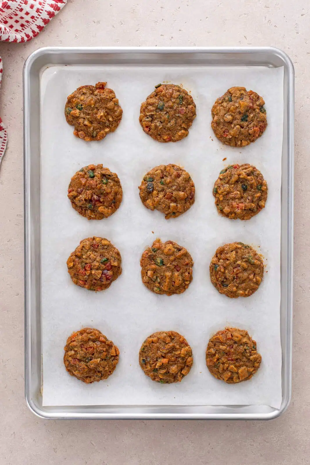 Baked fruitcake cookies resting on a baking sheet.