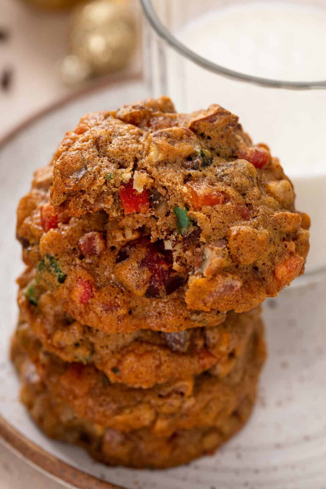 Stacked fruitcake cookies on a plate, with a bite taken from the top cookie.