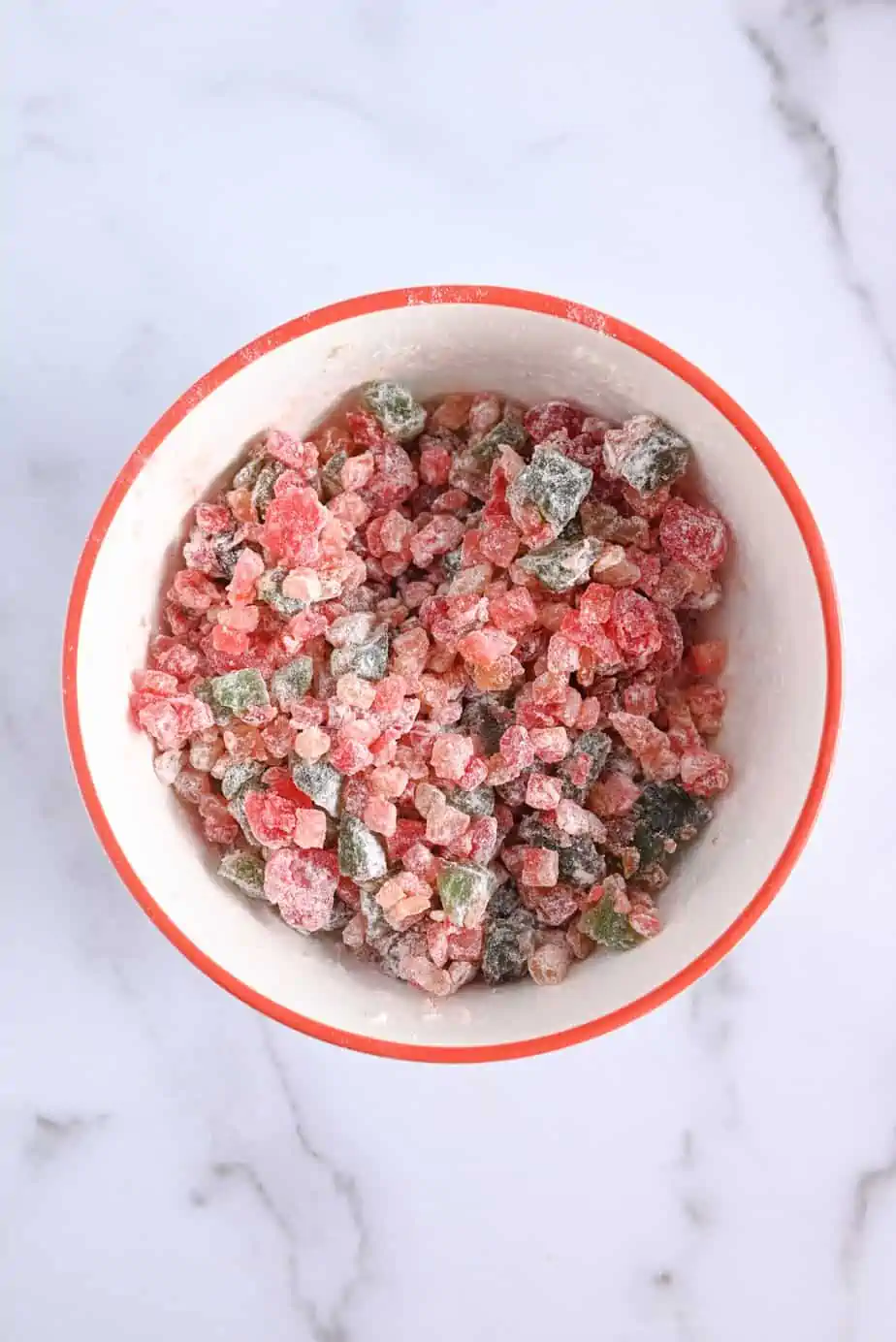 Chopped candied fruitcake fruit tossed with flour in a white bowl.