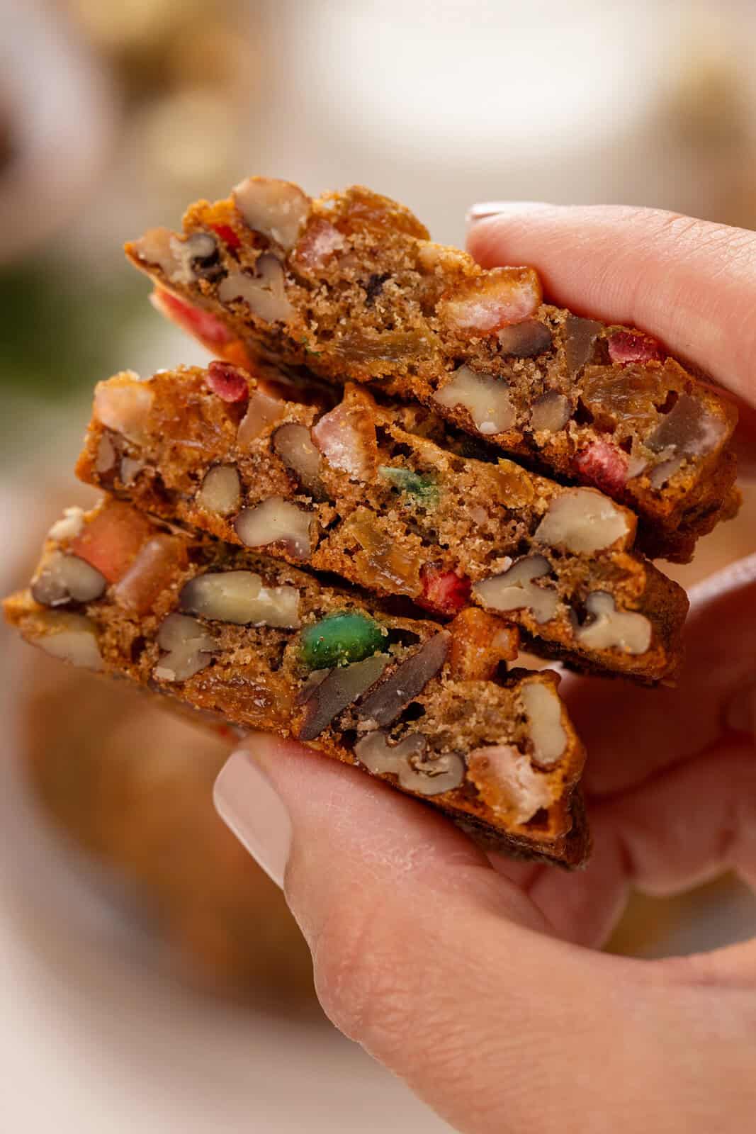 Hand holding 3 halved fruitcake cookies to show in the inside texture.