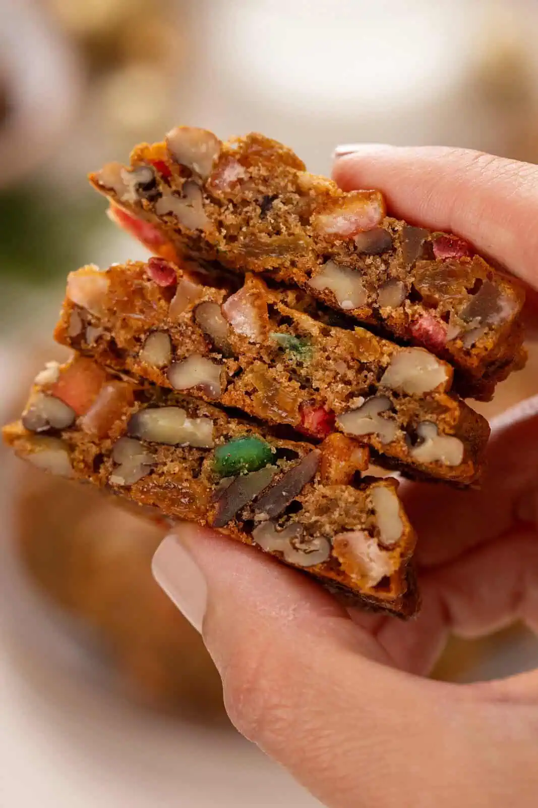 Hand holding 3 halved fruitcake cookies to show in the inside texture.