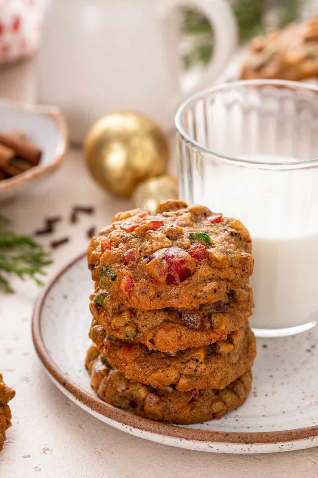 Four fruitcake cookies stacked on a plate in front of a glass of milk.